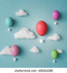 Hot air balloons made of decorated Easter eggs with cotton clouds on bright blue background. Flat lay. Creative concept.
