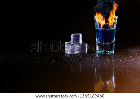 Hot alcoholic cocktail burning in shot glass with ice cubes.