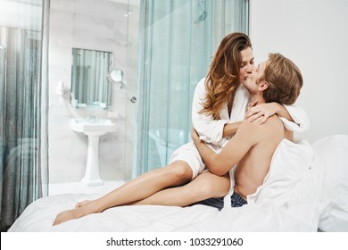 Hot Attractive Girlfriend Sits On Boyfriend While Kissing And Hugging Him Tenderly In Bed. Foreplay Moment Of Two People In Relationship, Spending Time In Hotel Room That Fills With Sexual Tension.