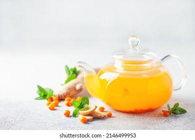 Hot autumn tea with sea buckthorn, ginger and mint in a glass teapot on a gray background - Shutterstock ID 2146499953