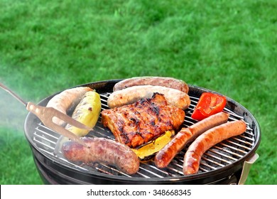 Hot BBQ Grill With Ribs, Bratwurst And Sausages, Close Up, Top View. Green Lawn In The Background. Outdoor Party or Picnic Concept.