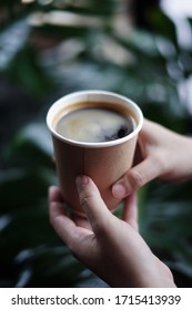 hot black coffee americano in hand with green plant on background