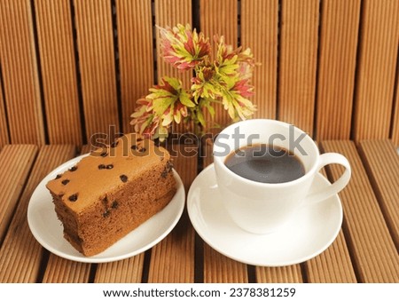 Hot black coffee with a large chocolate raisin egg snack on the side. On the brown slatted floor


