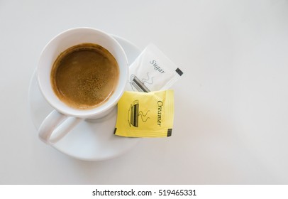 Hot Black Coffee In White Cup With Cream And Sugar In Packet On White Table 