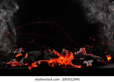 Hot burning coals on barbecue tray on black background with sparks and white smoke