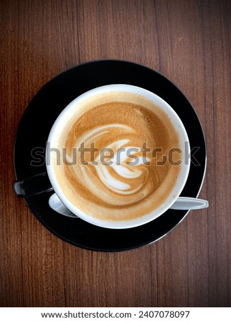Hot cafe latte espresso coffee in black ceramic cup with rosetta latte art isolated on brown background