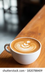 Hot Cappuccino Coffee With Heart Shaped Latte Art In A White Ceramic Cup On Warm Brown Wooden Counter Table - Perspective View