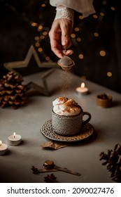Hot cappuccino coffee mug on a table decorated with milk foam, candles. Holiday Merry Christmas mood food photo. Cinnamon falling in the cup - Shutterstock ID 2090027476