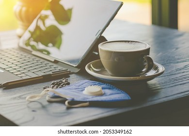 Hot Cappuccino Coffee With Protective Face Mask For People Work From Home By Using Laptop And Stress Relief With Hot Coffee On A Table. Concepts Of Covid-19 (Coronavirus). Selective Focus On Coffee.