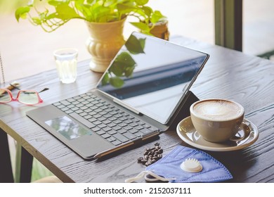 Hot Cappuccino Coffee With Protective Face Mask For People Work From Home By Using Laptop And Stress Relief With Hot Coffee On A Table. Concepts Of Covid-19 (Coronavirus). Selective Focus On Coffee.