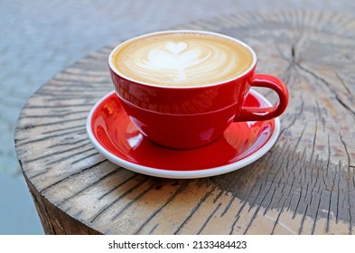 A Hot Cappuccino Coffee In Red Cup Served On Tree Stump Table