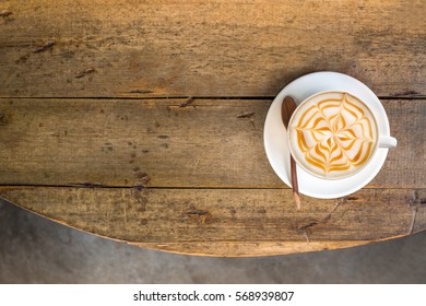 Hot Cappuccino Coffee With Zigzag Caramel Motif Or Spiderweb Art Topping On Wooden Old Round Table Background. Coffee Break At Retro Style Coffee Shop, Top View.