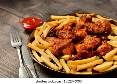 Hot chicken wings and french fries with ketchup and mustard. food lunch or dinner, typical fast food. on a wooden background. food delivery concept. selective focus and copy space