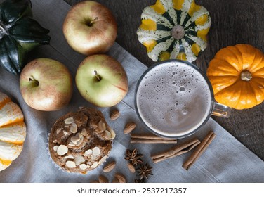 Hot chocolate in a glass mug paired with a spiced apple and almond muffin surrounded with pumpkins of various shapes - Powered by Shutterstock