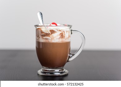 Hot chocolate in glass mug with whipped cream and a cherry