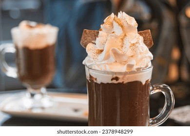 Hot chocolate with whipped cream and golden edible glitter in a transparent cup. Blurred background.