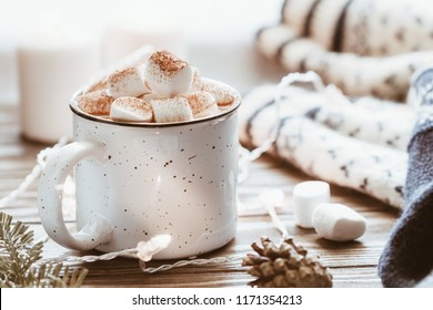 Hot cocoa with marshmallow in a white ceramic mug surrounded by winter things on a wooden table. The concept of cosy holidays and New Year. 