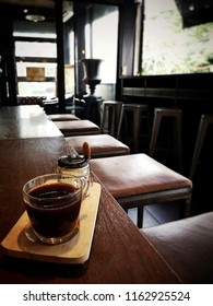 Hot Coffee (Caffe Americano) With Coffee Creamer In Glass Jar On Wooden Table Counter Bar With Chairs In Cafe And Restaurant