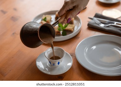 Hot coffee in a cezve. Turkish and Arabic style of making coffee. A woman's hand pours hot coffee into an Arabic cup.Selective focus, close-up - Powered by Shutterstock