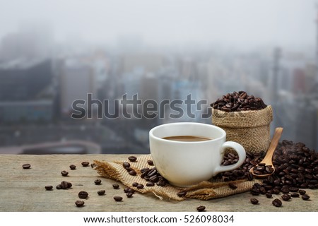 Hot coffee cup with coffee bean roating on the wooden table and the city background with copy space