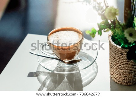 Hot Coffee cup and coffee beans on glass bottom plate(saucer) and  blur and soft sun light natural background.(vintage and soft tone concept)