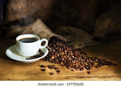 Hot Coffee cup and roast coffee beans on a wooden table and sack background
