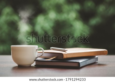 Hot coffee, smoke, with books and pen for note taking with beautiful nature background.