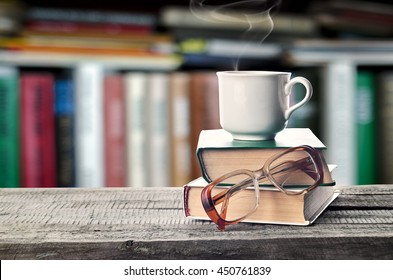 Hot coffee or tea, cocoa, chocolate cup on book and eyeglasses with copy space for text against the background of a bookshelf. Pile of books, glasses and cup on a table in the library - Powered by Shutterstock