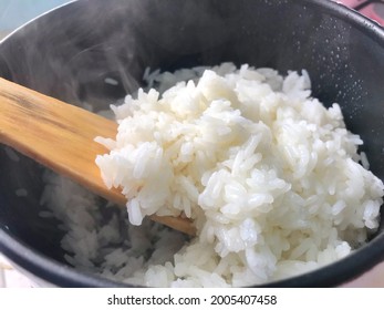 Hot Cooked Rice, A Pot With A Brown Wooden Spoon Was Scooping Up The Rice. Hot Steam Coming Out