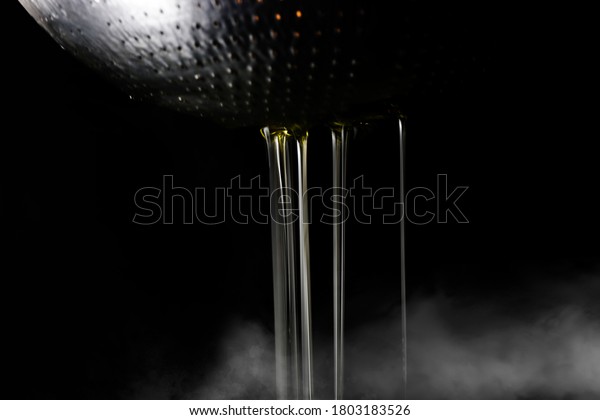 Hot cooking oil\
dripped through a hole in a colander and there was smoke from below\
on dark background