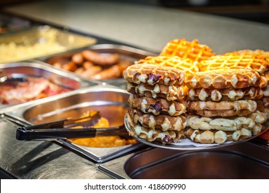 Hot counter containing warm breakfast items such as scrambled or fried tomatoes, waffles, bacon, sausages and others in a self service restaurant in a hotel