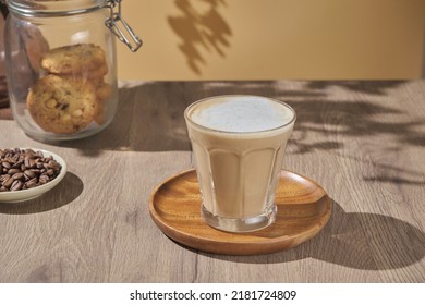 hot creamy milk in coffee is served with cookies. hot latte coffee drink in glass with cream milk on wooden table.  breakfast beverage morning concept.