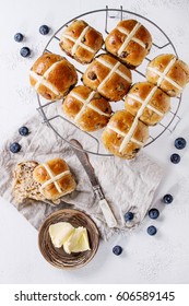 Hot cross buns on baking rack served with butter, fresh blueberries, knife and jug of cream on textile napkin over white texture concrete background. Top view, space. Easter baking.