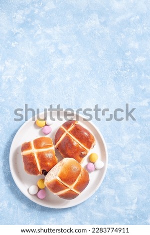 Hot cross buns on white plate with chocolate candy eggs. Traditional easter food, vertical, top view