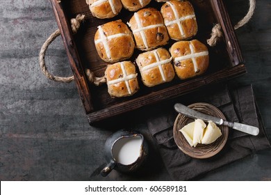 Hot cross buns in wooden tray served with butter, knife and jug of cream on textile napkin over old texture metal background. Top view, space. Easter baking.