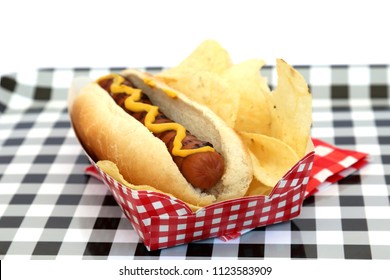 Hot Dog. Hot Dog In Bun And Potato Chips With Mustard Squiggle On A Black And White Checker Serving Tray. Isolated On White. Room For Text. 