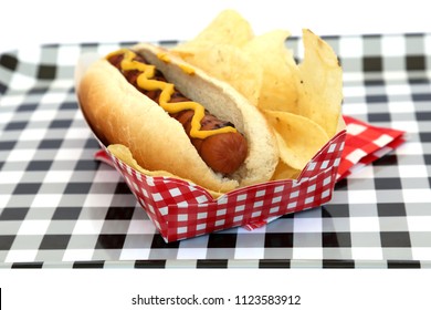 Hot Dog. Hot Dog In Bun And Potato Chips With Mustard Squiggle On A Black And White Checker Serving Tray. Isolated On White. Room For Text. 