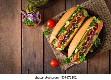 Hot dog with  pickles, tomato and lettuce on wooden background. Top view