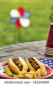 Hot Dogs At A July 4th Cookout Are Dressed With Ketchup And Mustard And Are Served With Potato Chips And A Pickle.  Selective Focus Was Used On This Image Which Is One In A Patriotic Series.