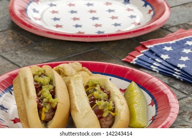 Hot Dogs At A July 4th Cookout Are Dressed With Ketchup, Mustard And Relish And Are Served With Potato Chips And A Pickle.  Selective Focus Was Used On This Image Which Is One In A Patriotic Series.