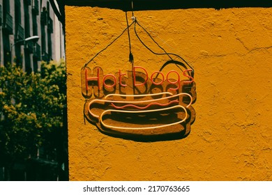 Hot Dogs LED Sign Against Yellow Wall On Street. Fast Food Bistro, Cafe Stylish Exterior. Hot Dog Modern Trendy Neon Label, Icon. Design Element, Light Banner, Announcement. USA, American Food Snacks