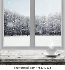 Hot drink in cup on table over winter forest background through window view