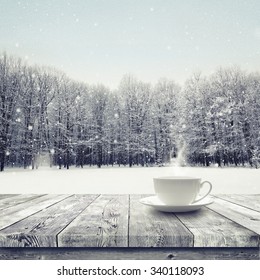 Hot Drink In The Cup On Wooden Table Over Winter Snow Covered Forest. Beauty Nature Background