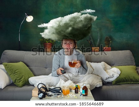 Hot drink. Ill young girl with fever and cold feeling sick, blue, snuffling. Big cloud above the head like weight during feeling ill. Cold, virus, seasonal grippe. Woman sitting on sofa at home.