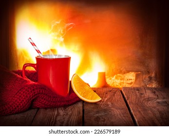 Hot Drink In A Red Mug And Orange Slice On Vintage Wood Table. Fireplace As Background. Christmas Or Winter Warming Drink. Layout With Free Text Space.