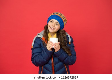 Hot Drink For Winter Morning. Small Girl Hold Tea Cup Red Background. Happy Child With Winter Look. Hot Chocolate Weather. Food And Drink. Stay Warm In Winter. Winter Can Be Warm.