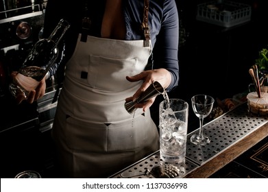 Hot female barman with neckline pouring gin into a cocktail glass for making fresh summer cocktail