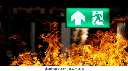 Hot flame fire and green fire escape sign hang on the ceiling in the Warehouse at night. The concept of fire escape training and preparation for evacuation