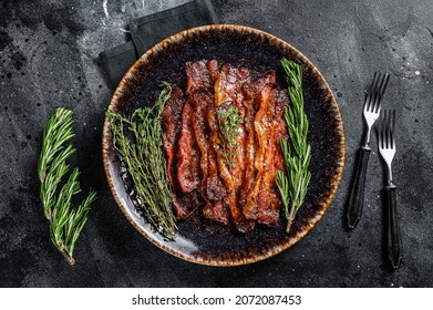 Hot Fried crunchy Bacon sizzling slices in plate with herbs. Black background. Top view