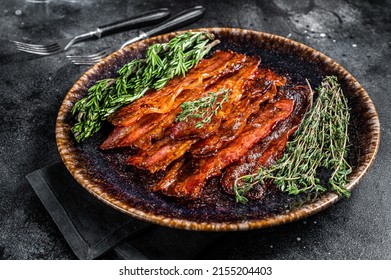 Hot Fried crunchy Bacon sizzling slices in plate with herbs. Black background. Top view.